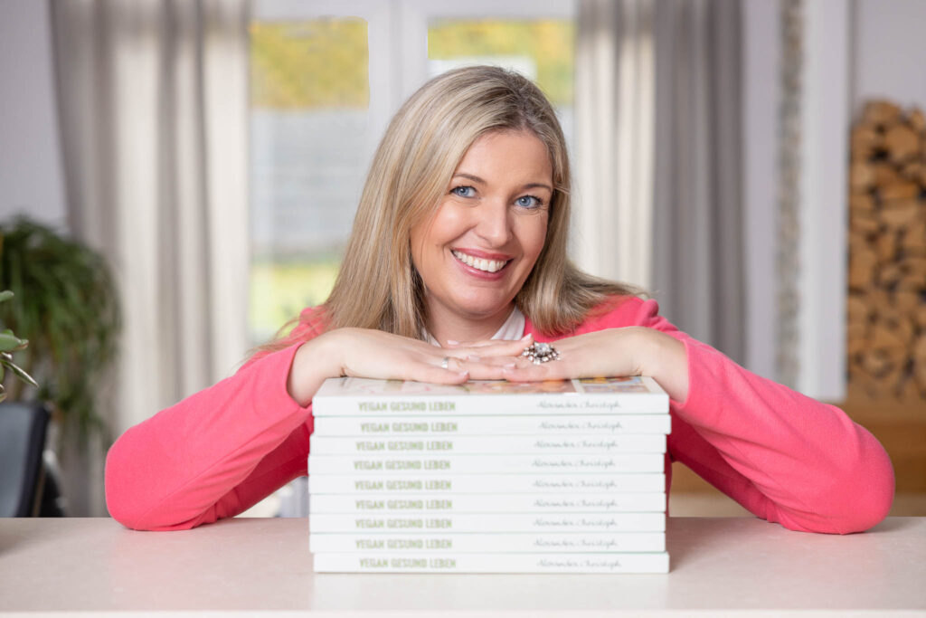 Alexandra Christoph in pinkem Jacket, Personal Branding Portrait mit ihrem eigenen Buch als Stapel - in Koblenz