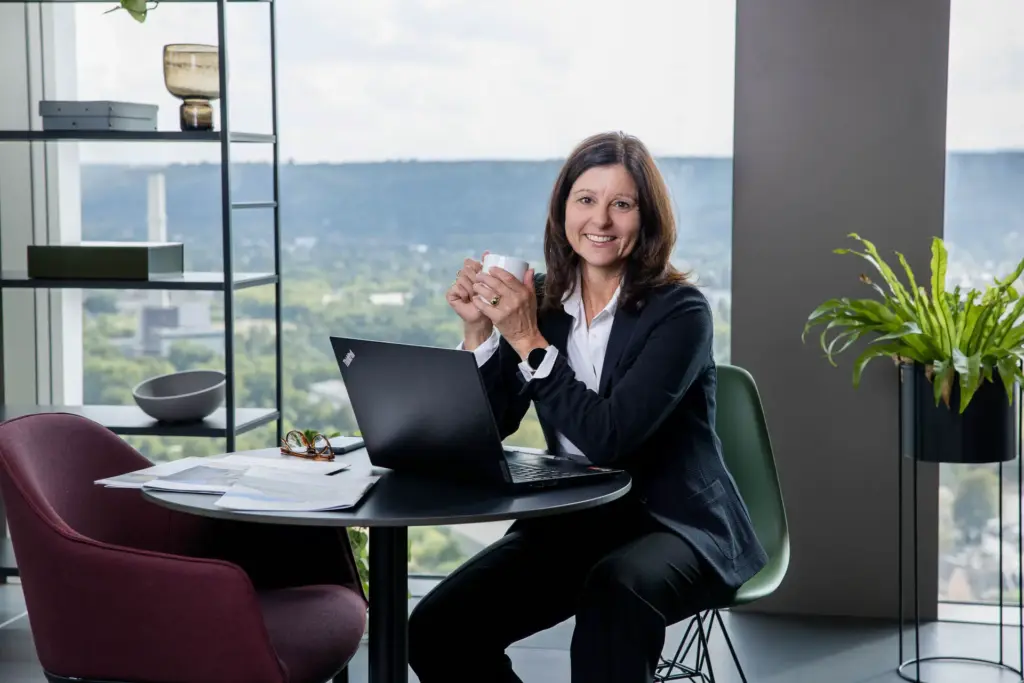 Personal Branding Fotos in Bonn - Immobilienmaklerin Claudia Ewens in der 27. Etage am Kanlerplatz weit über Bonn mit Kaffeetasse und Laptop