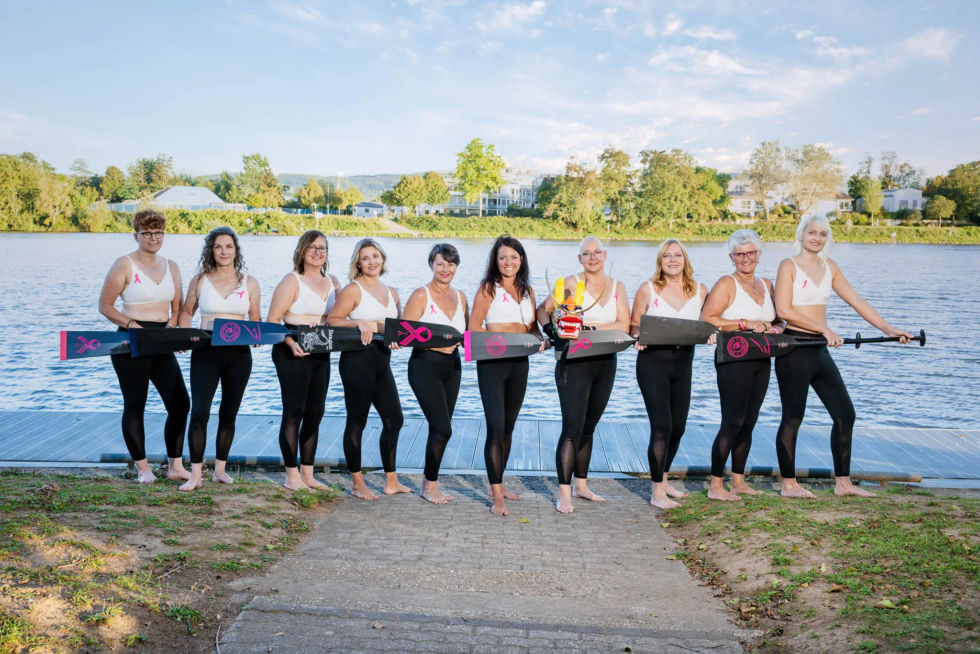 Zehn Frauen der Pink Paddler in weißen BH's im Drachenboot Ohana auf der Mosel – Symbolbild für Stärke, Zusammenhalt und Sichtbarkeit.