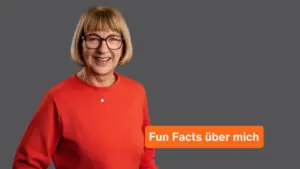 Karina Schuh, Markenfotografin aus Polch bei Koblenz, lacht in die Kamera — orangefarbener Pullover, Brille, grauer Hintergrund.