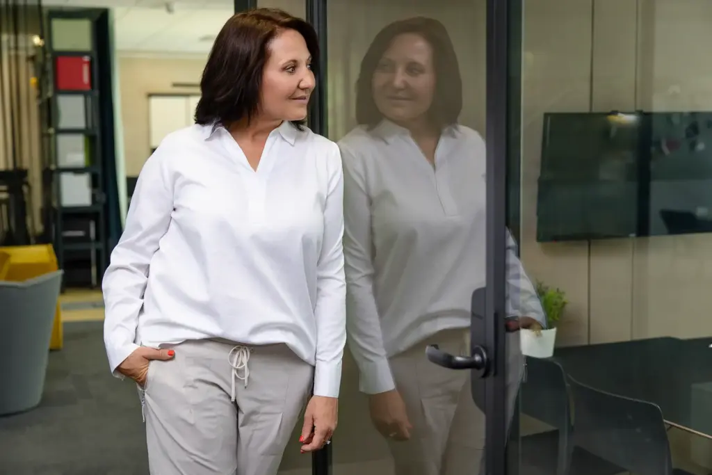 Unternehmerin im weißen Hemd lehnt an Glastür – kreatives Business-Portrait mit Spiegelung