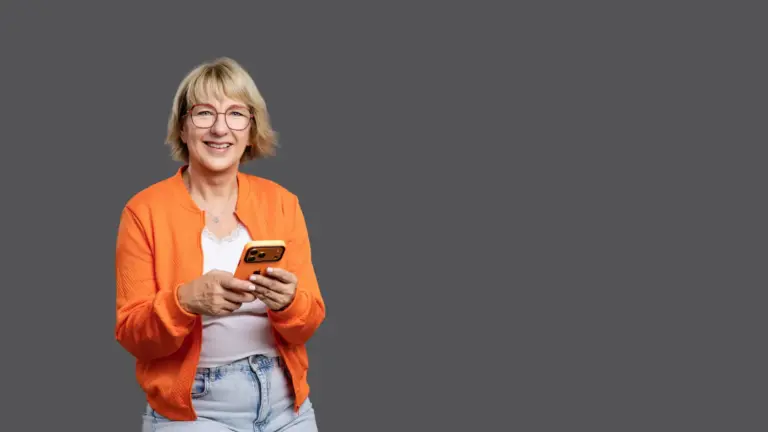 Kontakt zu Karina Schuh, Markenfotografin mit Studio in Polch bei Koblenz. Karina Schuh trägt eine orangefarbene Jacke und hält ein orangenes Smartphone in der Hand.