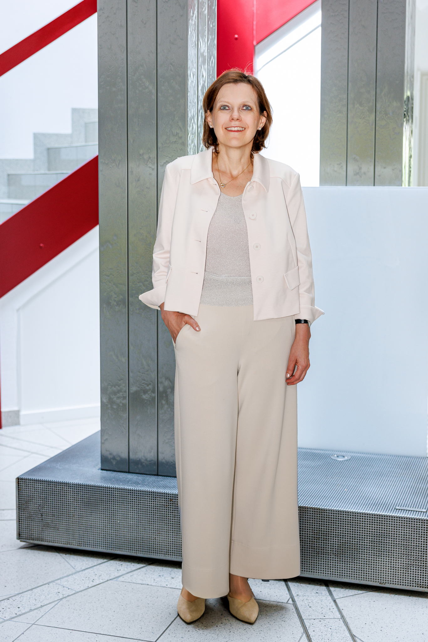 Portrait von Prof. Dr. Michaela Seybold in cremefarbenem Outfit vor der Säule mit dem Springbrunnen im Gebäude