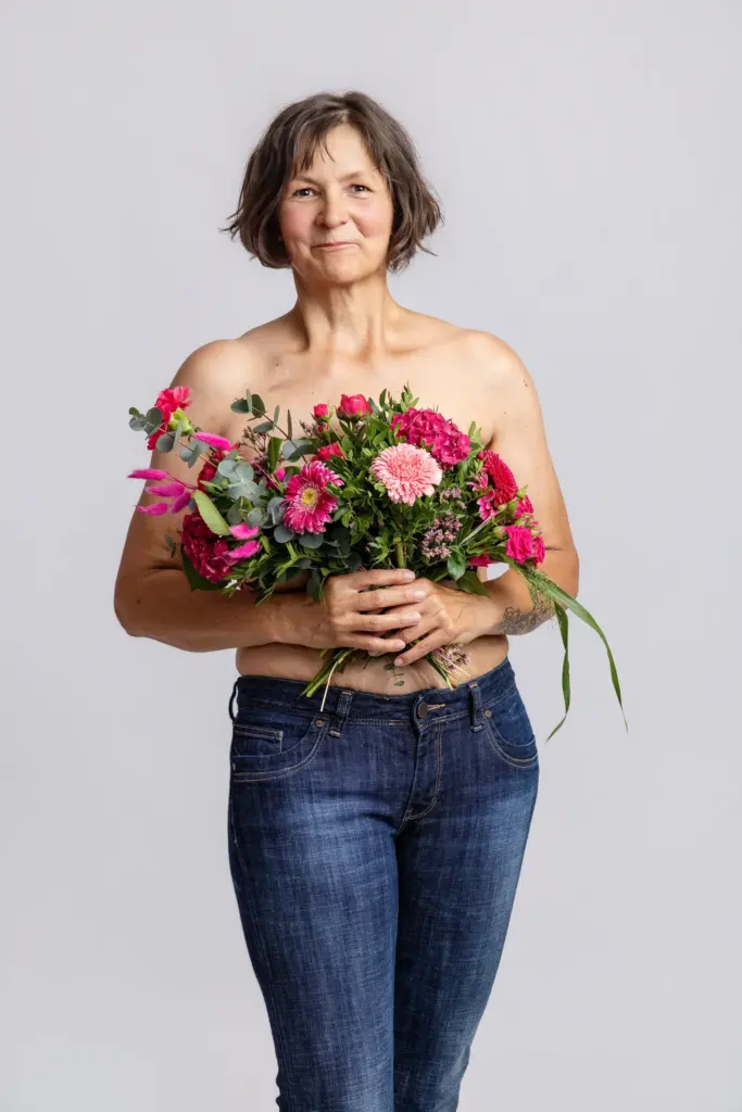 Frau mit lockigen Haaren in Jeans hält einen pinken Blumenstrauß vor der Brust, Portrait für Pinktober Koblenz 2026