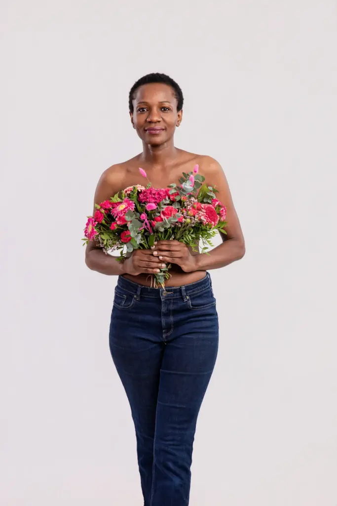 Lächelnde Frau in dunkler Jeans mit pinkem Blumenstrauß vor der Brust, Portrait für die Pinktober-Kampagne Koblenz 2026