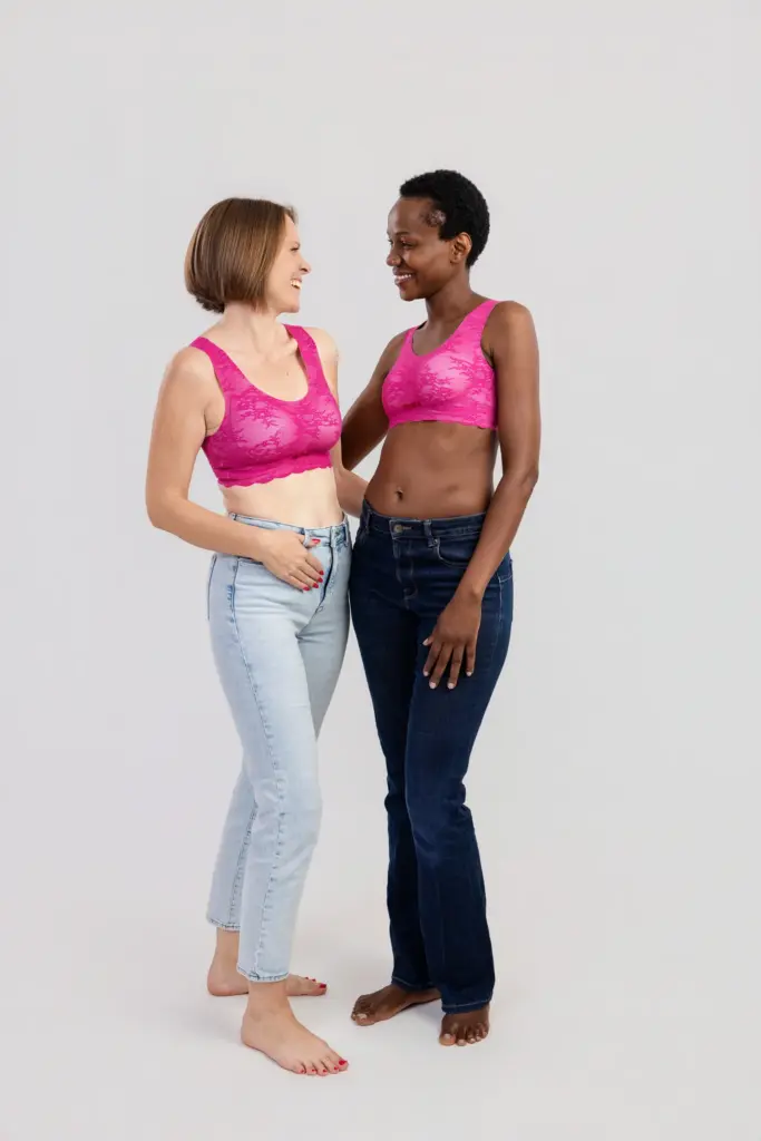 Zwei lächelnde Frauen in pinken BHs und Jeans stehen barfuß Arm in Arm im Studio, Pinktober Koblenz 2026