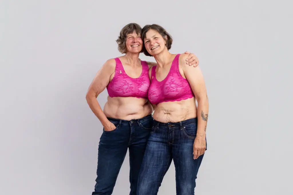Gudrun und Sigrid in pinken BHs halten sich im Arm und zeigen selbstbewusst ihre Narben, Pinktober Koblenz 2026