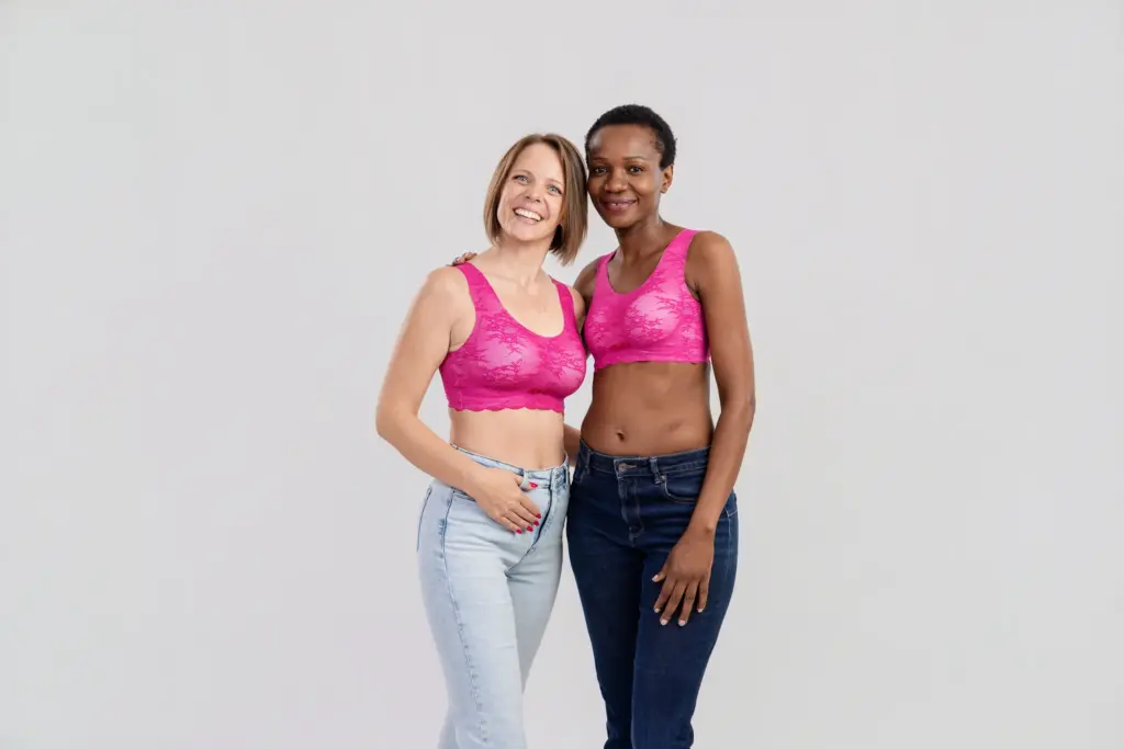 Zwei strahlende Frauen in pinken BHs und Jeans stehen eng nebeneinander, Pinktober Koblenz 2026