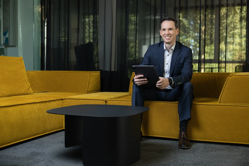 Steuerberater Tobias Junges sitzt mit Tablet auf einem gelben Sofa bei designfunktion, Businessfotos für die Website